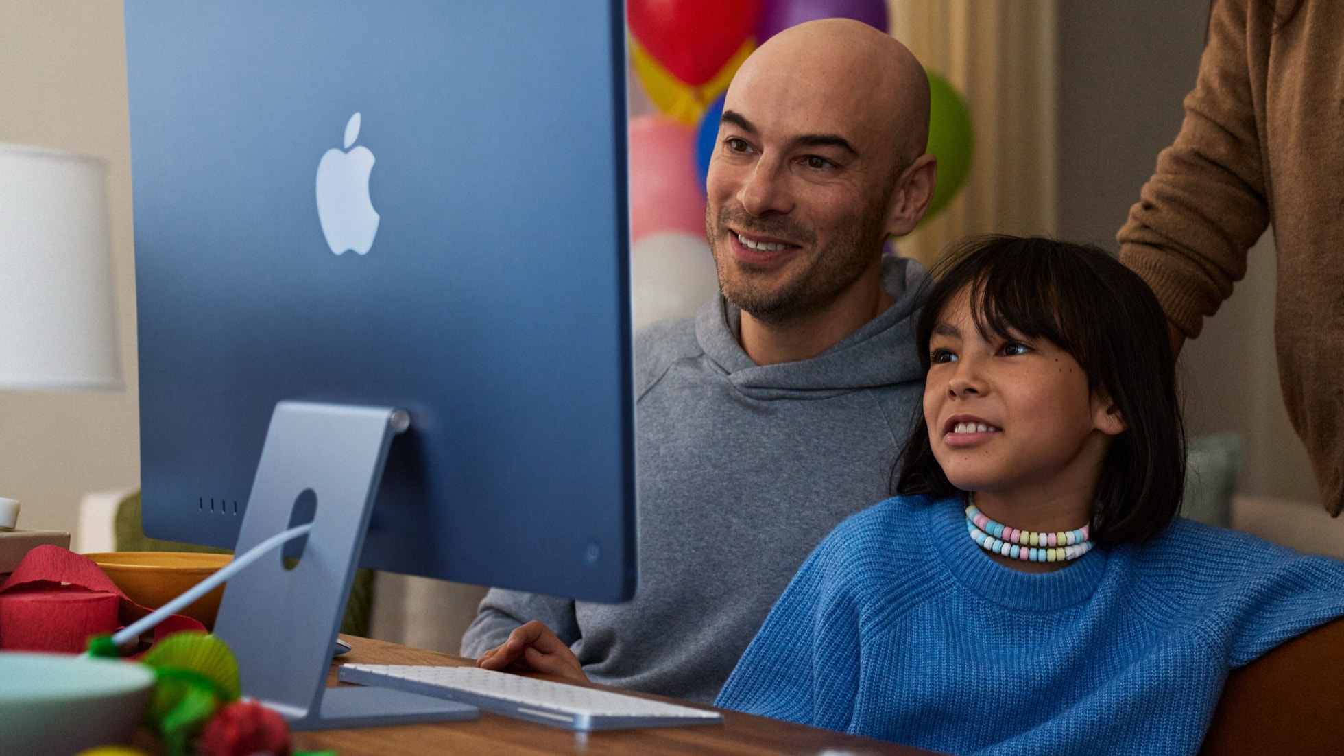 A child uses an iMac while two adults supervise nearby.