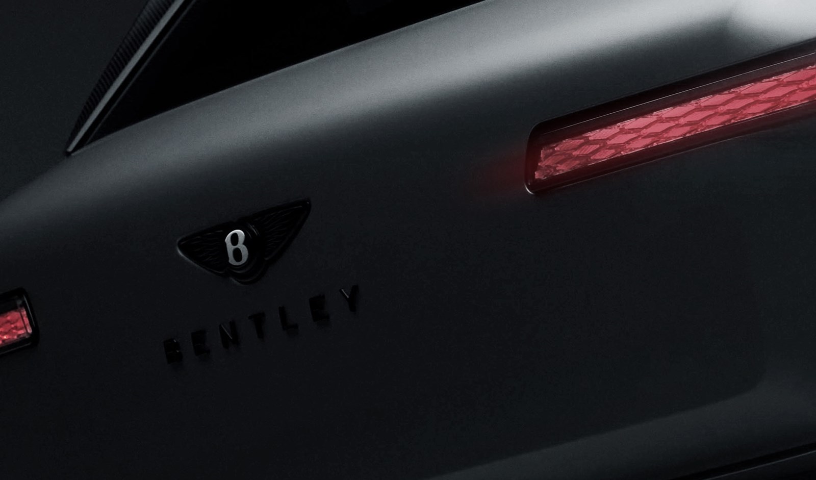 Official Bentley teaser image showing the dark rear detail and illuminated tail lamps of the Torcal electric SUV.