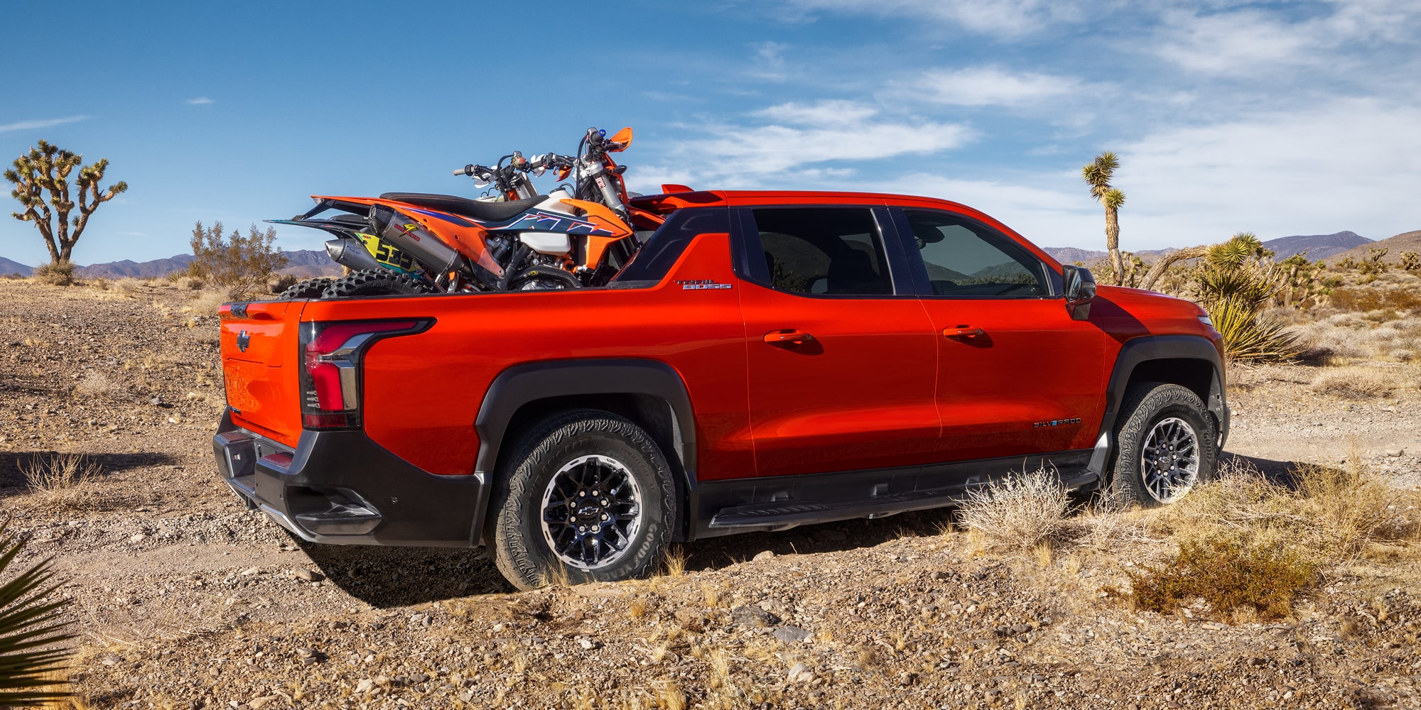 Orange 2026 Chevrolet Silverado EV shown carrying a dirt bike in an official Chevrolet image.