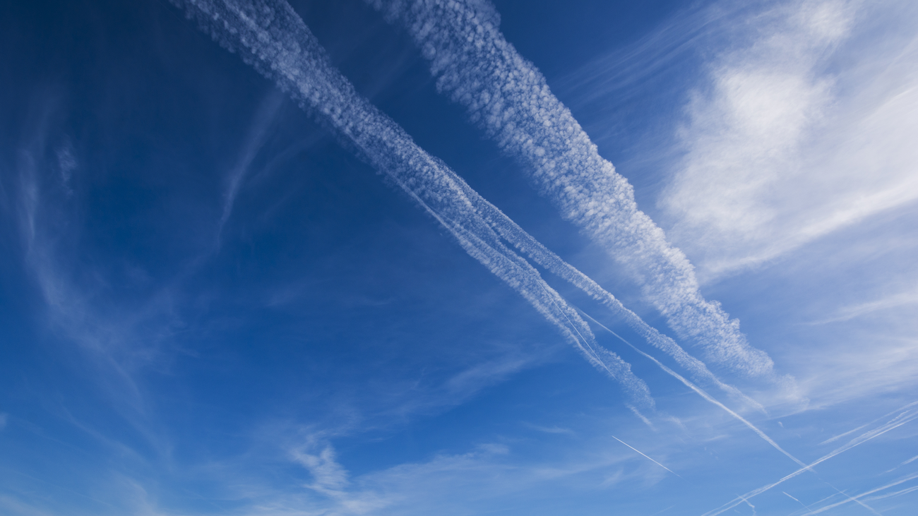 A commercial jet flying above clouds with a white contrail trailing behind it.