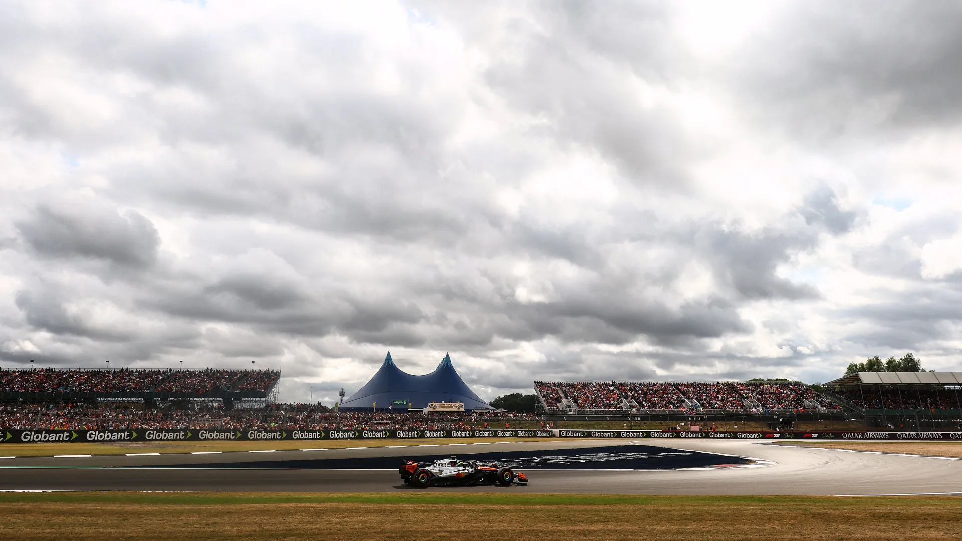 A Formula 1 car running at Silverstone under cloudy skies.