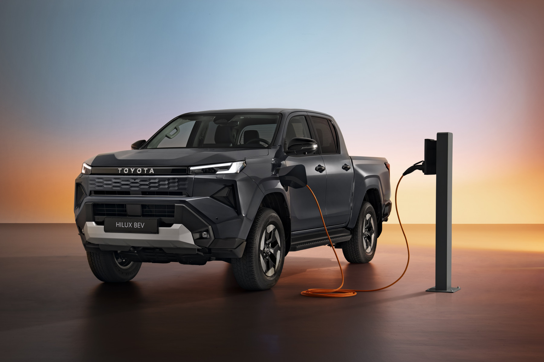 Toyota Hilux BEV shown plugged into a charger in an official studio product image.